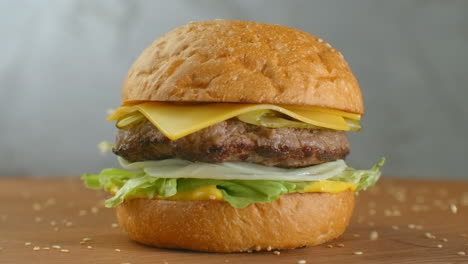 In-slow-motion-sesame-seeds-fall-on-a-spinning-hamburger.-Hamburger-on-a-wooden-Board