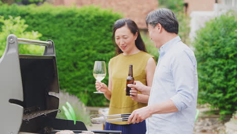 Mature-Couple-Cooking-Outdoor-Barbeque-And-Drinking-Wine-And-Beer-At-Home