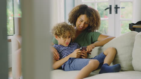 Mutter-Und-Sohn-Sitzen-Zu-Hause-Auf-Dem-Sofa-Und-Spielen-Gemeinsam-Ein-Videospiel-Auf-Dem-Handy