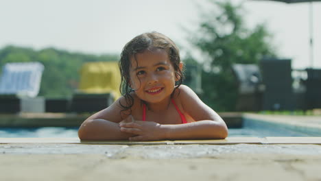 Portrait-Of-Young-Girl-Looking-Over-Edge-Of-Outdoor-Pool-And-Sticking-Out-Tongue-On-Vacation