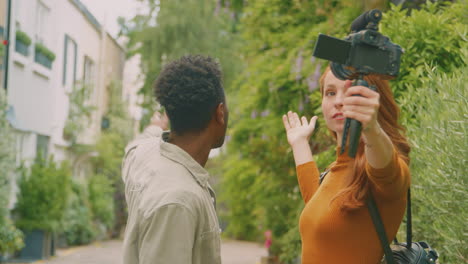 Young-Couple-Travelling-Through-City-Together-Vlogging-To-Video-Camera-In-Park