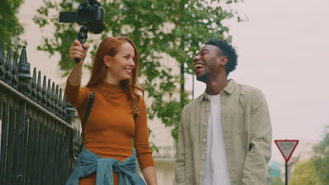 Pareja-Joven-Viajando-Juntos-Por-La-Ciudad-Haciendo-Vlogging-Con-Una-Cámara-De-Video-En-Un-Trípode