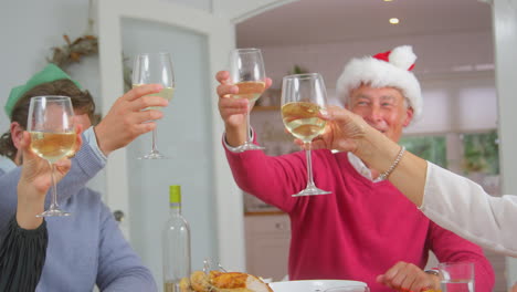 Adultos-Haciendo-Brindis-Con-Vino-Mientras-Una-Familia-Multigeneracional-Come-Juntos-Una-Comida-Navideña