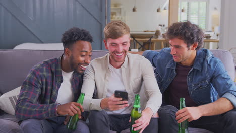 Grupo-Multicultural-De-Amigos-Varones-En-El-Sofá-De-Casa-Bebiendo-Cerveza-Y-Mirando-El-Teléfono-Móvil