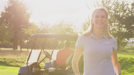 Portrait-Of-Smiling-Mature-Female-Golfer-Standing-By-Buggy-On-Golf-Course-With-Lens-Flare
