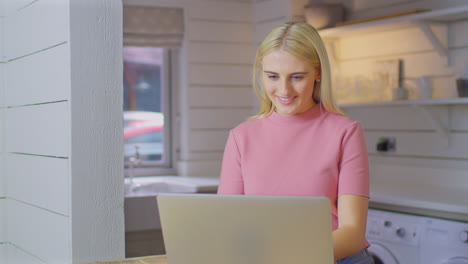Young-Woman-Standing-At-Kitchen-Counter-With-Laptop-Working-From-Home