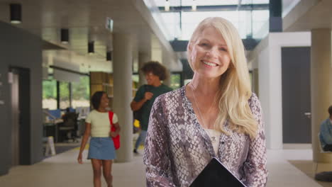 Portrait-Of-Smiling-Mature-Female-Tutor-In-Busy-University-Or-College-Building-With-Students