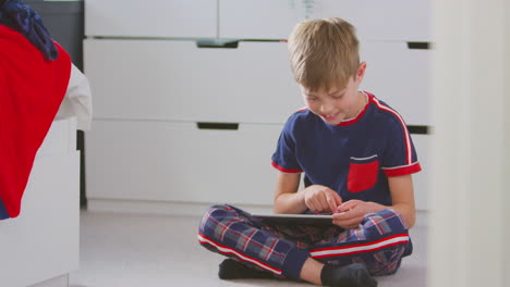 Junge-Zu-Hause-Im-Schlafzimmer-Trägt-Pyjamas-Und-Spielt-Auf-Einem-Digitalen-Tablet,-Das-Auf-Dem-Boden-Sitzt