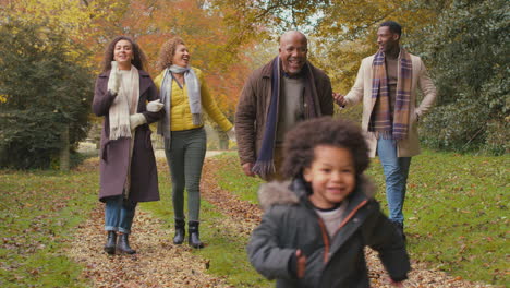 Lächelnde-Mehrgenerationenfamilie,-Die-Spaß-Mit-Kindern-Hat,-Die-Gemeinsam-Durch-Die-Herbstliche-Landschaft-Spazieren