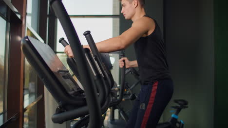 Un-Hombre-De-Fitness-Retrato-Se-Calienta-Antes-De-Entrenar-En-Una-Bicicleta-Elíptica-En-El-Gimnasio.-Ejercicio-Cardiovascular-De-Entrenamiento-Masculino-De-Primer-Plano-En-Bicicleta-Cruzada-En-Fitness