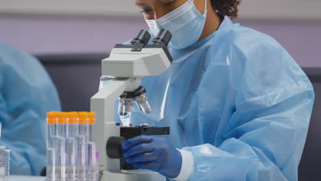 Female-Lab-Worker-Wearing-PPE-Analysing-Slide-And-Focusing-Microscope