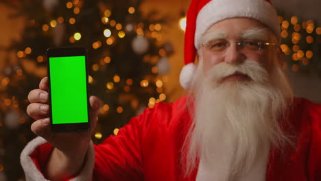 Santa-Señala-Con-El-Dedo-La-Pantalla-Verde-Del-Teléfono-Móvil.-Venta-De-Navidad.-El-Anciano-Papá-Noel-Muestra-Una-Pantalla-Con-Un-Cromakey.-Imágenes-4k-De-Alta-Calidad