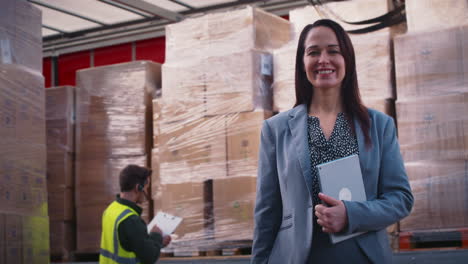 Portrait-Of-Smiling-Female-Freight-Haulage-Manager-Standing-By-Lorry-Being-Loaded-With-Boxes
