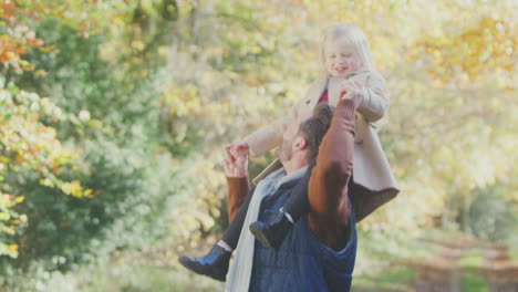 Father-Playing-Game-Carrying-Daughter-On-Shoulders-On-Family-Walk-Along-Track-In-Autumn-Countryside