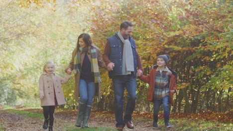Family-With-Mature-Parents-And-Two-Children-Holding-Hands-Walking-Along-Track-In-Autumn-Countryside