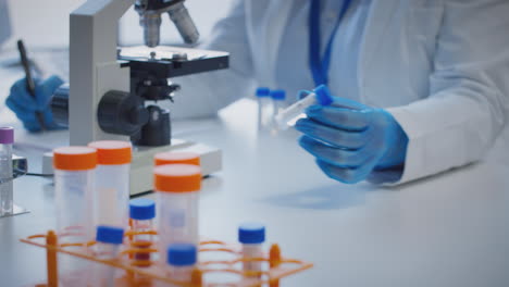 Close-Up-Of-Lab-Worker-Conducting-Research-Using-Microscope-Holding-Test-Tube-Labelled-Xi