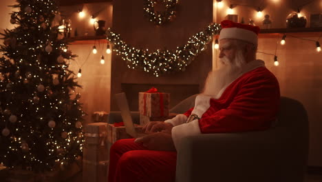 Santa-Claus-is-working-on-a-laptop-sitting-at-home-on-the-sofa-in-the-background-of-Christmas.-Santa-responds-to-children-emails.-High-quality-4k-footage