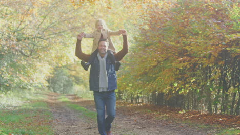 Father-Playing-Game-Carrying-Daughter-On-Shoulders-On-Family-Walk-Along-Track-In-Autumn-Countryside