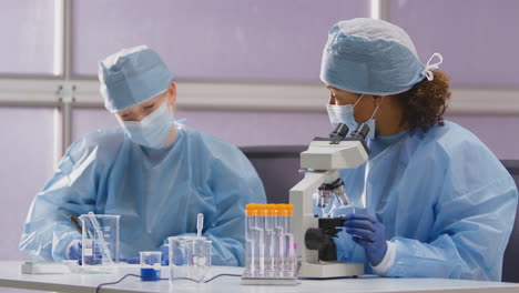Weibliche-Labormitarbeiter-Tragen-PSA-Und-Analysieren-Proben-Im-Labor-Mit-Mikroskop,-Um-Testergebnisse-Aufzuzeichnen