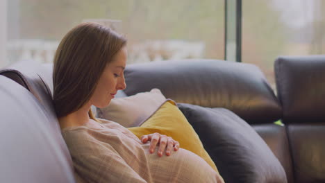 Mujer-Embarazada-Relajándose-Sentada-En-El-Sofá-De-Casa-Viendo-La-Televisión