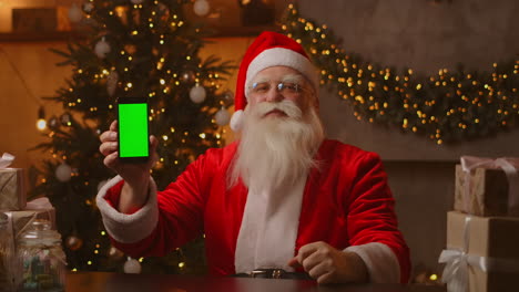 Der-Weihnachtsmann-Zeigt-Mit-Dem-Finger-Auf-Den-Grünen-Bildschirm-Des-Mobiltelefons.-Weihnachtsverkauf.-Der-ältere-Weihnachtsmann-Zeigt-Einen-Bildschirm-Mit-Einem-Chromakey.-Hochwertiges-4K-Filmmaterial