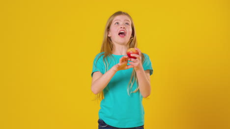 Studioporträt-Eines-Mädchens,-Das-Apfel-Und-Orange-Vor-Gelbem-Hintergrund-Jongliert
