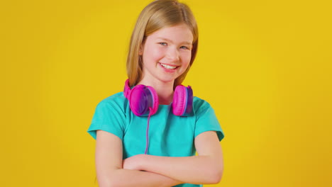 Studioporträt-Eines-Mädchens,-Das-Kopfhörer-Trägt-Und-Vor-Gelbem-Hintergrund-In-Die-Kamera-Lächelt