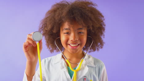 Studio-Portrait-Of-Boy-Dressed-As-Doctor-Or-Surgeon-With-Stethoscope-Against-Purple-Background