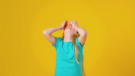 Studioporträt-Eines-Mädchens,-Das-Zwei-Orangefarbene-Hälften-Vor-Den-Augen-Vor-Gelbem-Hintergrund-Balanciert