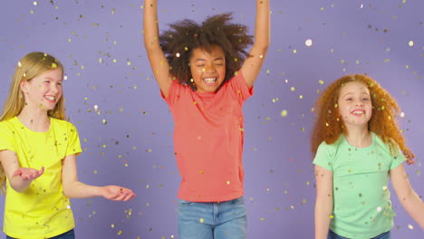 Studio-Shot-Of-Children-With-Glitter-Jumping-In-The-Air-With-Outstretched-Arms-On-Purple-Background