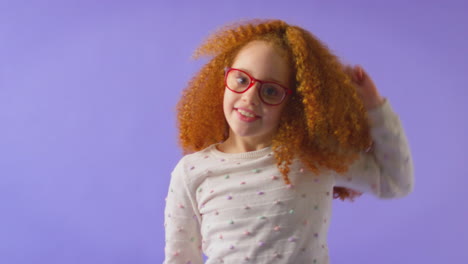 Studio-Shot-Of-Energetic-Girl-Wearing-Red-Glasses-Jumping-And-Dancing-Against-Purple-Background