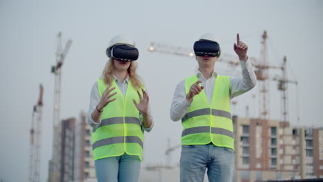 Dos-Personas,-Hombre-Y-Mujer,-Con-Gafas-De-Realidad-Virtual-En-El-Fondo-De-Edificios-En-Construcción-Con-Grúas.-Gerente-Y-Asistente-De-Diseño-Con-Las-Manos-Imitando-La-Interfaz-De-La-Aplicación