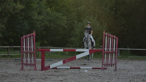 Eine-Jockeyin-Im-Schwarz-weißen-Anzug-Auf-Einem-Pferd-Macht-Einen-Sprung-über-Die-Barriere.-Zeitlupe:-Eine-Jockeyin-Im-Schwarz-weißen-Anzug-Auf-Einem-Pferd-Macht-Einen-Sprung