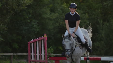 Young-female-rider-on-bay-horse-jumping-over-hurdle-on-equestrian-sport-competition