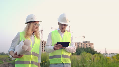 Zwei-Wirtschaftsingenieure-Tragen-Schutzhelme-Und-Halten-Ein-Tablet-In-Der-Hand.-Sie-Arbeiten-Als-Ingenieure-Und-Besprechen-Die-Inspektion-Von-Zeichnungen.-Draußen-An-Einem-Gebäude.-Technische-Werkzeuge.