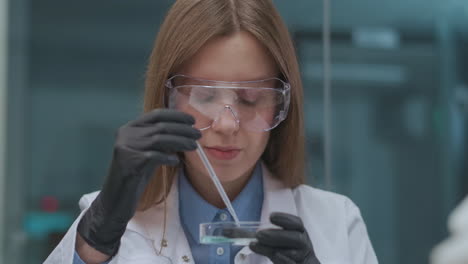 Estudiante-Del-Instituto-Químico-Está-Haciendo-Trabajo-Práctico-En-Clase-Retrato-De-Una-Mujer-Joven-Con-Gafas-Protectoras,-Guantes-De-Goma-Y-Bata-Blanca-Explorando-Reactivo