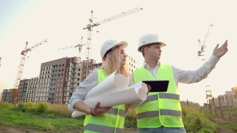 Zwei-Wirtschaftsingenieure-Tragen-Schutzhelme-Und-Halten-Ein-Tablet-In-Der-Hand.-Sie-Arbeiten-Als-Ingenieure-Und-Besprechen-Die-Inspektion-Von-Zeichnungen.-Draußen-An-Einem-Gebäude.-Technische-Werkzeuge.