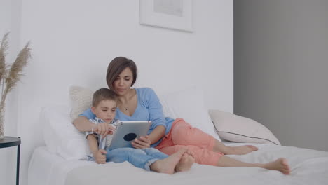 Madre-E-Hijo-Usando-Tableta-Digital-En-El-Dormitorio-De-Casa.-Vista-Frontal-De-Una-Feliz-Madre-E-Hijo-Caucásicos-Usando-Una-Tableta-Digital-En-El-Dormitorio-De-Casa