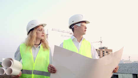 Trabajadores-Con-Dibujos-En-El-Sitio-De-Construcción.-Dos-Trabajadores,-Hombre-Y-Mujer,-Con-Sombreros-Protectores-Trabajando-Con-Dibujos-En-El-Sitio-De-Construcción-Al-Aire-Libre.