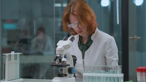 La-Doctora-Está-Explorando-El-Análisis-En-El-Laboratorio-Tomando-Una-Muestra-De-Líquido-Del-Tubo-De-Ensayo-Y-Mirando-En-El-Microscopio-A-Una-Mujer-Profesional-De-La-Salud-En-La-Clínica-De-Coronavirus