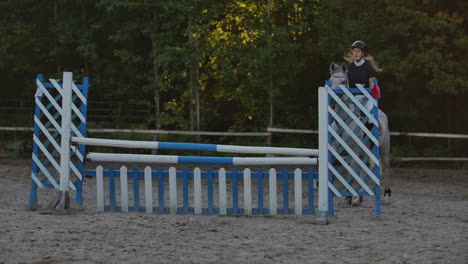 Young-female-rider-on-bay-horse-jumping-over-hurdle-on-equestrian-sport-competition