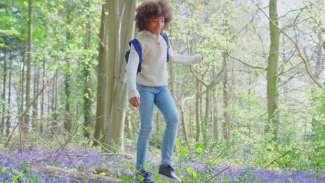 Two-Children-Walking-Through-Bluebell-Woods-In-Springtime-Balancing-On-Log