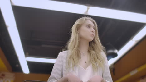 Pretty-lady-in-casual-clothes-is-walking-in-grocery-store-steering-shopping-trolley-with-food-inside-it-and-looking-around-at-shelves-with-products.-Women-and-shops-concept.