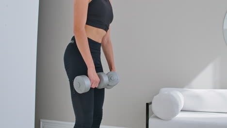 A-young-athletic-woman-in-a-bright-apartment-performs-a-deadlift-with-dumbbells-at-home-making-leans-forward-to-strengthen-the-muscles-of-the-thighs