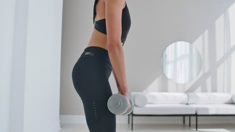 A-young-athletic-woman-in-a-bright-apartment-performs-a-deadlift-with-dumbbells-at-home-making-leans-forward-to-strengthen-the-muscles-of-the-thighs