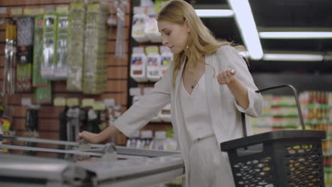 Business-woman-in-the-supermarket-takes-out-of-the-refrigerator-frozen-food-reads-the-composition-of-the-product-and-puts-it-in-the-basket.