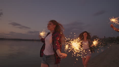 Eine-Gruppe-Von-Freunden,-Männern-Und-Frauen,-Feiert-Den-Feiertag-Fröhlich-Am-Strand-Mit-Wunderkerzen-Und-Feuerwerk.-Zeitlupen-Laufparty-In-Der-Nacht-Am-Strand.