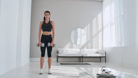 A-young-athletic-woman-in-a-bright-apartment-performs-a-deadlift-with-dumbbells-at-home-making-leans-forward-to-strengthen-the-muscles-of-the-thighs