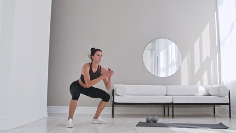 Mujer-Haciendo-Ejercicio-Saltando-Sentadillas-En-Casa.-Mujer-Sana-En-Ropa-Deportiva-Haciendo-Sentadillas-Saltando-En-Casa.-Mujer-Haciendo-Ejercicio-En-La-Sala-De-Estar