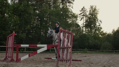 Young-woman-jumps-horse-over-an-obstacle-during-her-training-in-an-arena.-Young-woman-jumps-horse-over-an-obstacle-during-an-event-in-an-arena.-Sport.-Aims